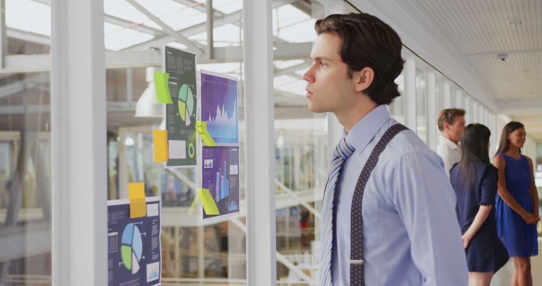 Young Businessman Analyzing Financial Charts on Office Glass Wall - Free Images, Stock Photos and Pictures on Pikwizard.com