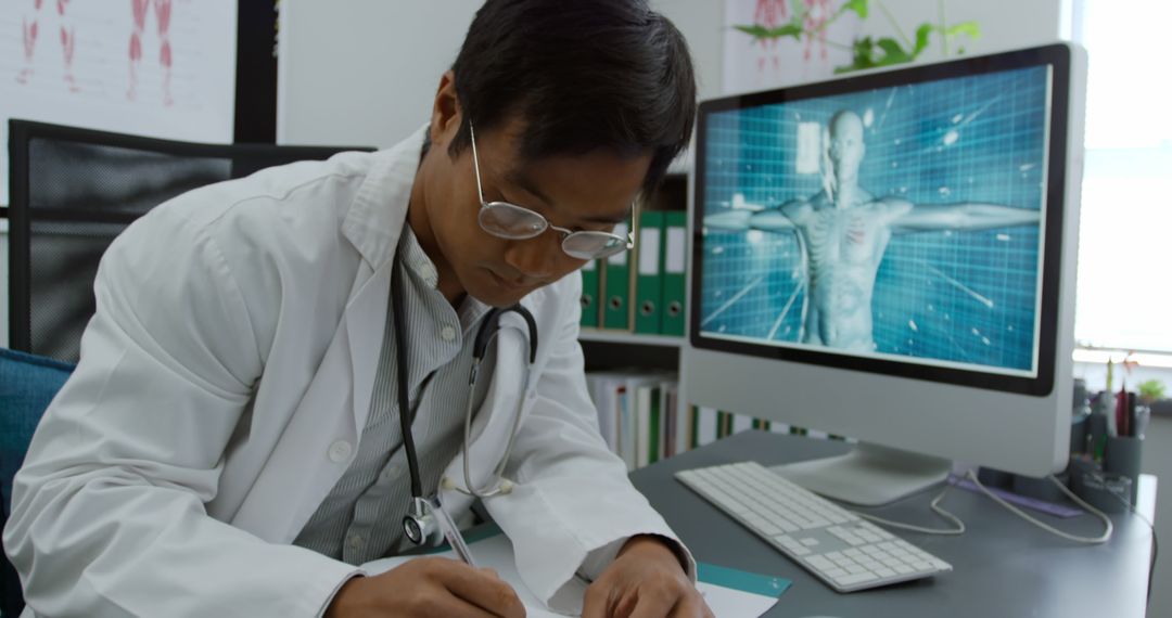 Doctor Writing Medical Notes at Desk with Anatomical Diagram on Computer Screen - Free Images, Stock Photos and Pictures on Pikwizard.com