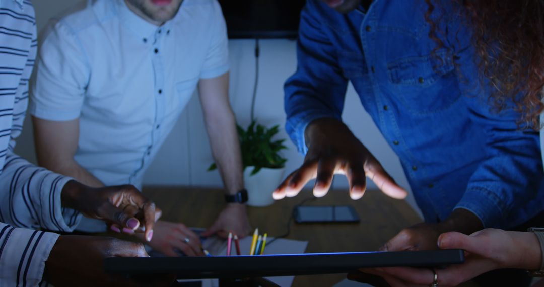 Diverse Group Collaborating on Tablet in Dimly Lit Room