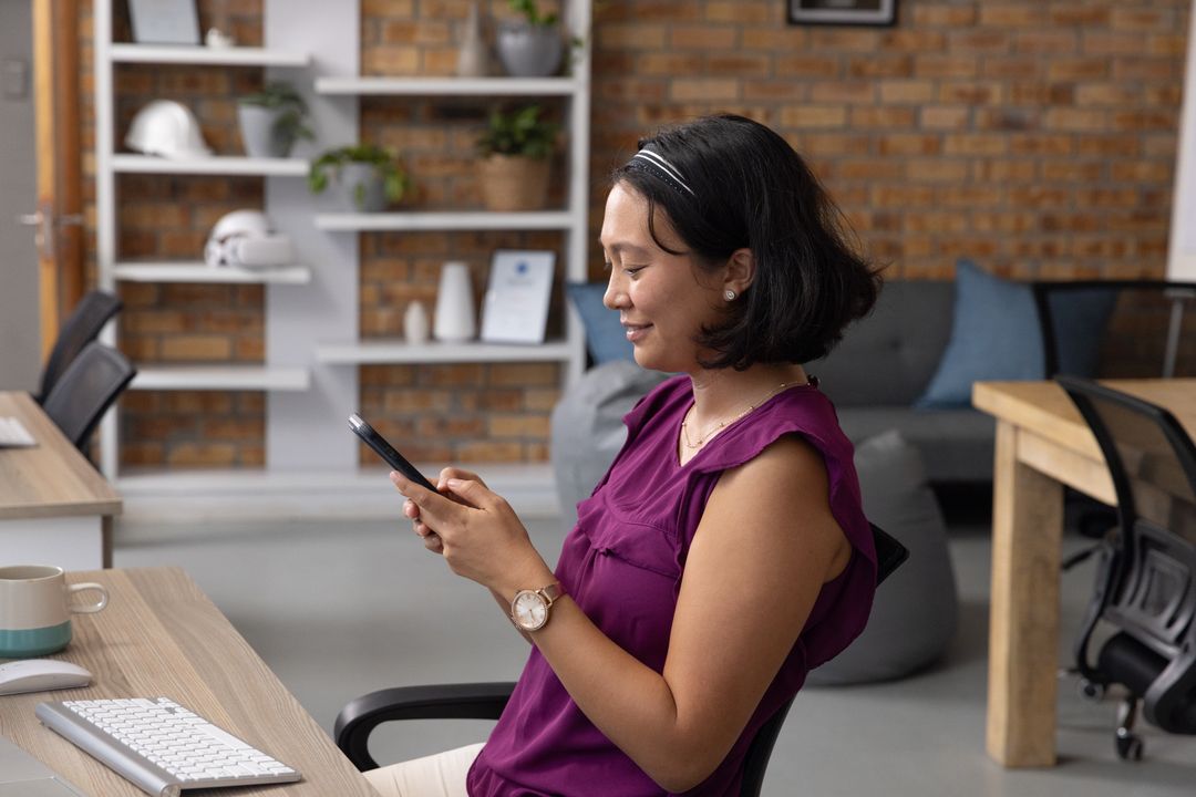 Asian Woman in Office Using Smartphone and Smiling
