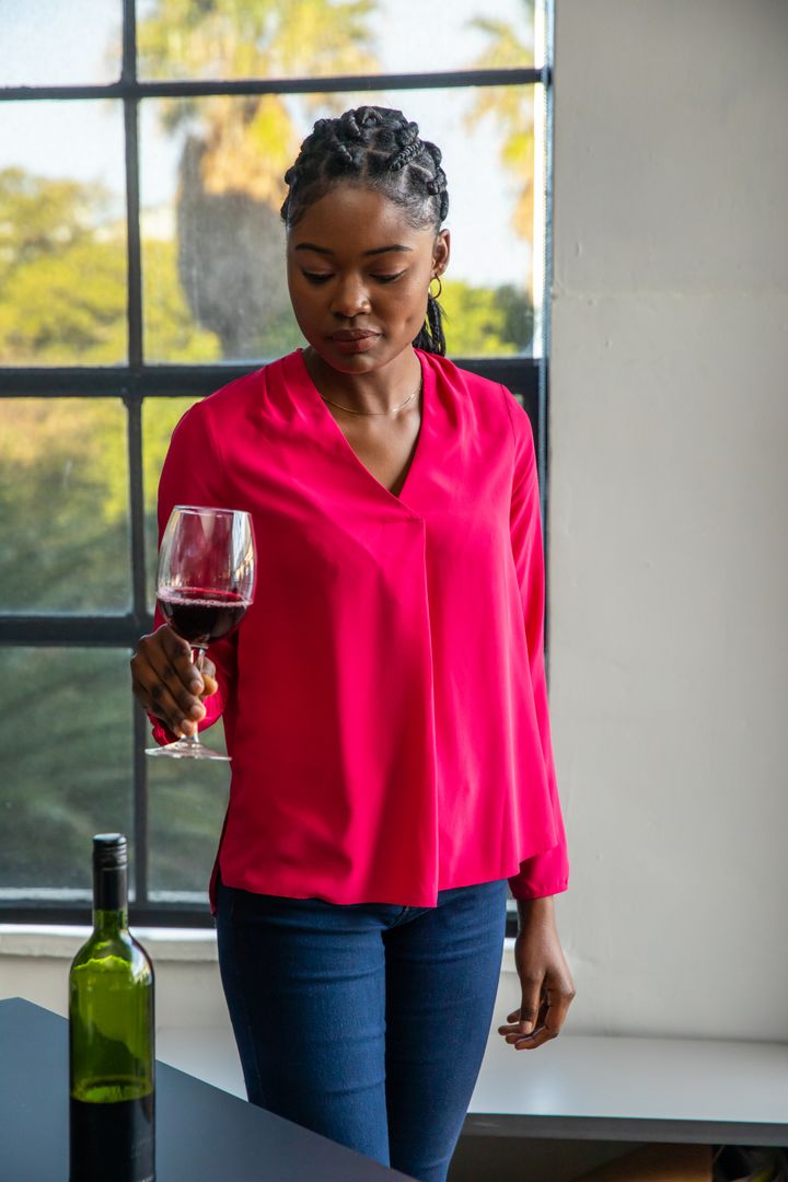 Woman in Bright Pink Blouse Enjoying Red Wine by Sunny Window