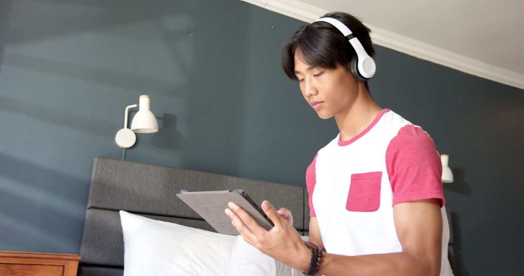 Teenage Boy Using Tablet and Headphones in Modern Bedroom