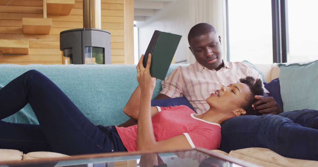 Image of happy african american couple sitting on sofa and reading together - Free Images, Stock Photos and Pictures on Pikwizard.com