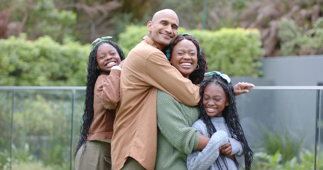African American family hugging and laughing on balcony with glass railing and garden