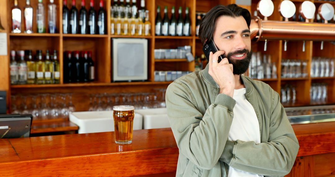 Man Chatting on Phone while Enjoying Beer at Bar