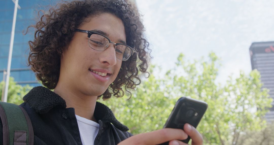 Young Man with Curly Hair Using Smartphone Outdoors - Free Images, Stock Photos and Pictures on Pikwizard.com