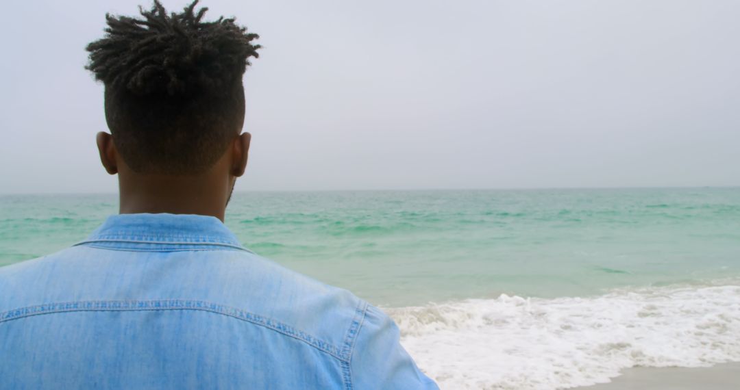 Man Gazing at Ocean Waves on Tranquil Beach Day