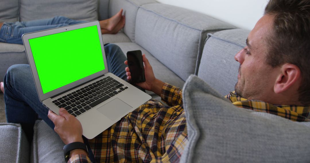 Man Relaxing on Couch Using Laptop and Phone with Green Screen - Free Images, Stock Photos and Pictures on Pikwizard.com