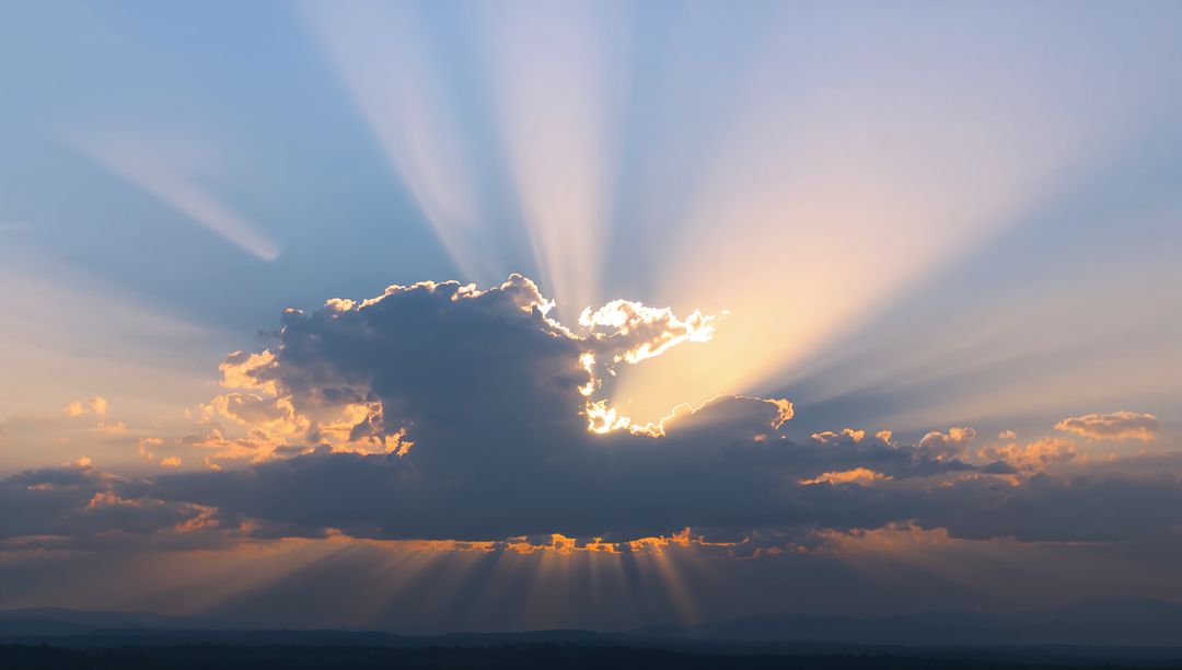 Sunbeams Radiating Behind Cumulus Cloud Over Low Hills During Sunset Glow