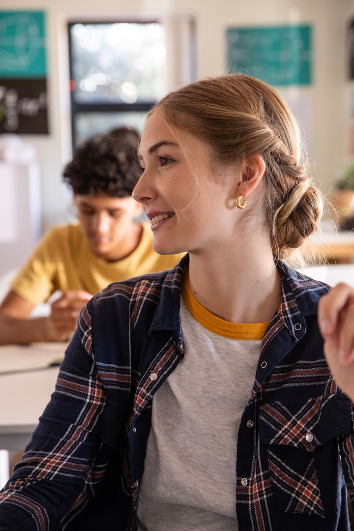 Female student listening in diverse classroom while classmates studying and writing notes