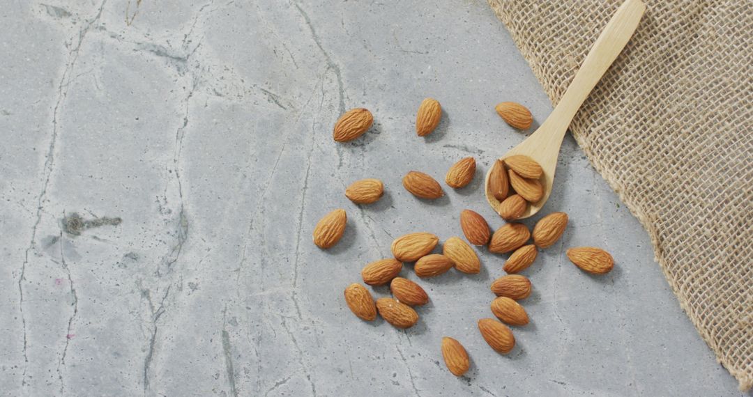 Pile of Raw Almonds on Rustic Stone with Jute and Wooden Spoon