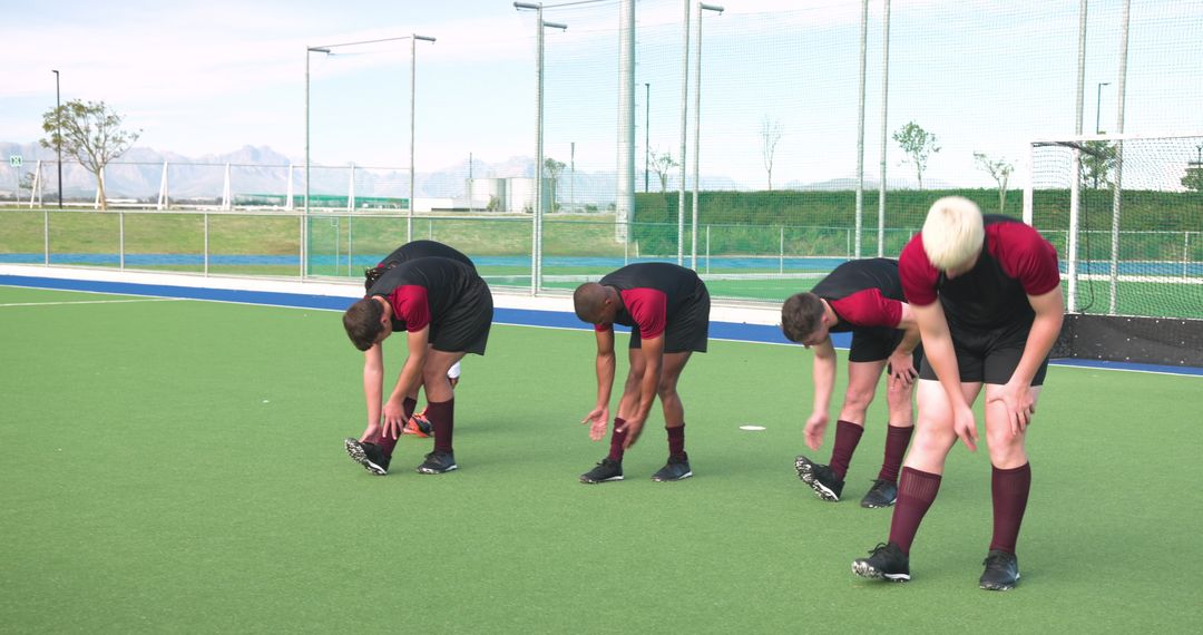 Diverse Teammates Stretching on Field Hockey Turf