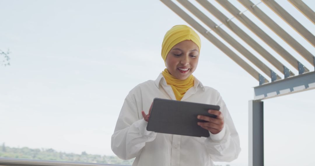 Muslim Woman in Yellow Hijab Using Tablet on Balcony - Free Images, Stock Photos and Pictures on Pikwizard.com