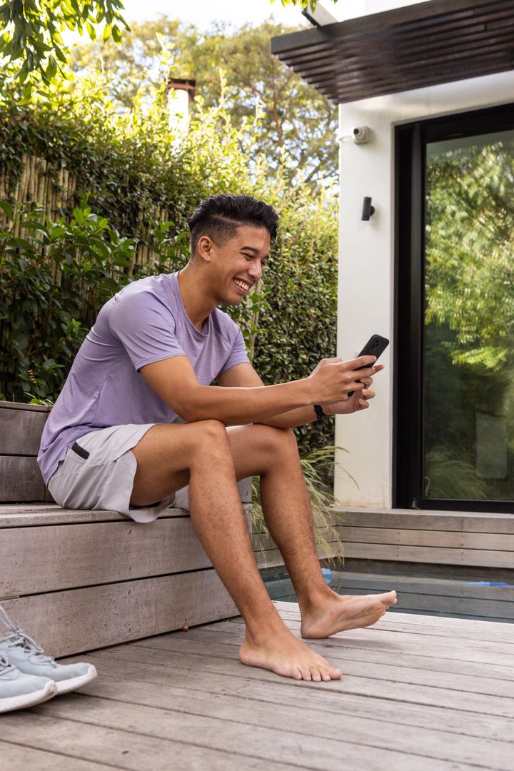 Asian Man Relaxing with Smartphone Outdoors on Modern Patio