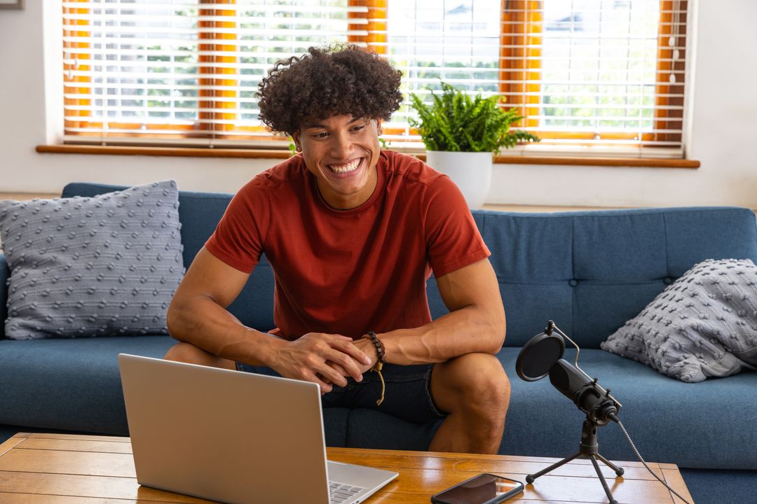 Smiling Young Man Podcasting at Home with Laptop and Microphone