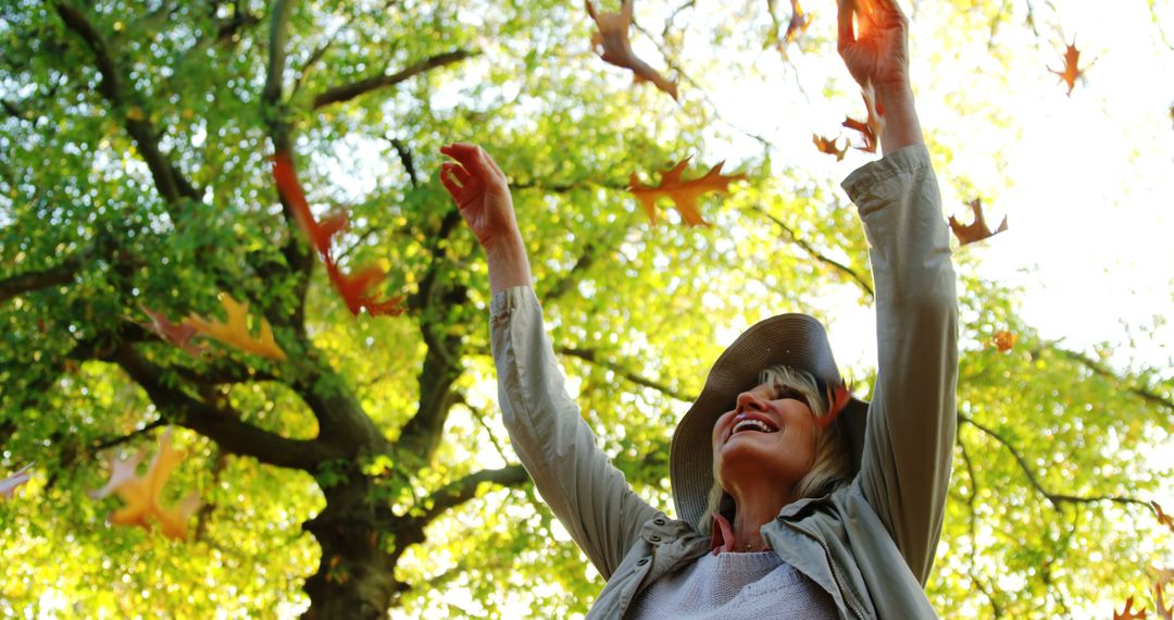 Senior Woman Enjoying Autumn Breeze Under Falling Leaves - Free Images, Stock Photos and Pictures on Pikwizard.com