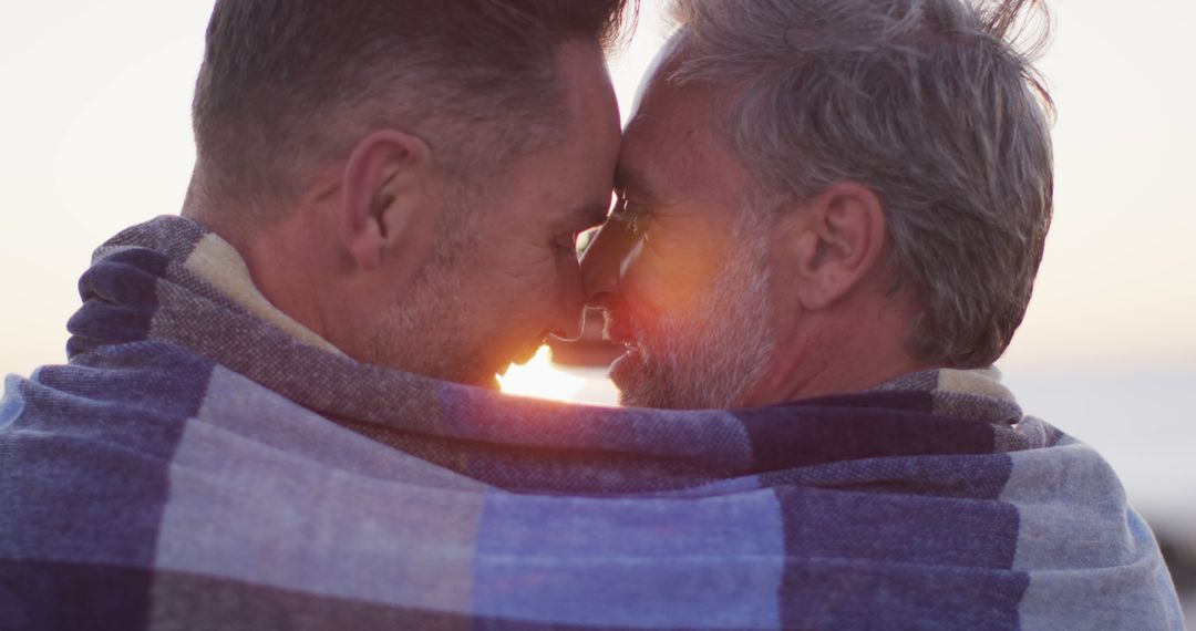 Happy caucasian gay male couple wearing blanket, embracing and taking selfie at sunset on the beach - Free Images, Stock Photos and Pictures on Pikwizard.com