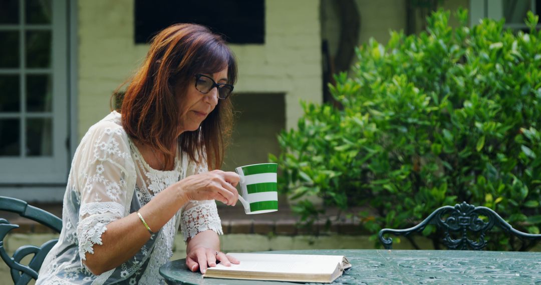 Middle-Aged Woman Reading Book and Drinking Coffee in Garden - Free Images, Stock Photos and Pictures on Pikwizard.com