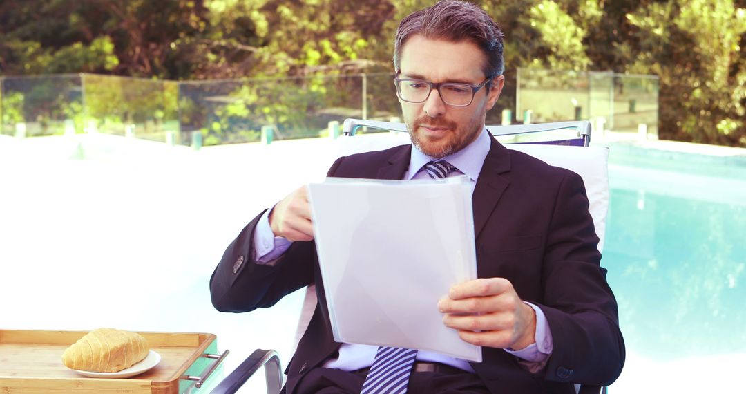 Businessman Reading Documents Poolside - Free Images, Stock Photos and Pictures on Pikwizard.com