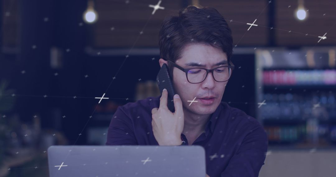 Focused Asian Man Multitasking With Laptop and Smartphone at Cafe