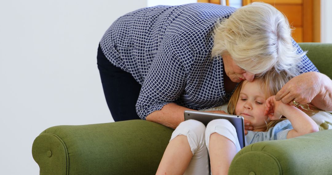 Grandmother Kissing Child's Forehead While Using Tablet on Couch - Free Images, Stock Photos and Pictures on Pikwizard.com