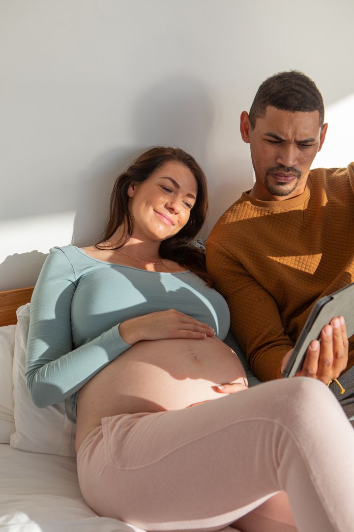 Expecting Couple Sharing Intimate Moment with Tablet in Bright Room