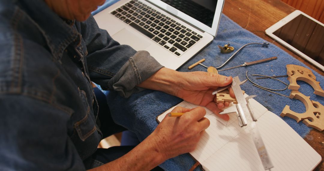 Woodworker using caliper while sketching designs near laptop and tablet - Free Images, Stock Photos and Pictures on Pikwizard.com