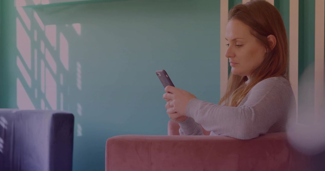 Casual woman scrolling smartphone on pink chair with teal wall shadows and copy space