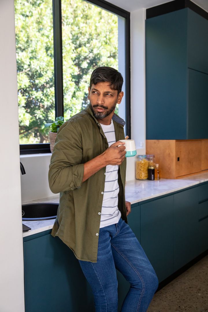 Man in Modern Kitchen Holding Mug Checking Smartphone Near Window