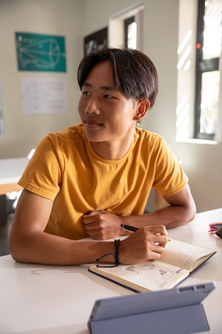 Asian Teen Student Studying in Classroom with Notebook