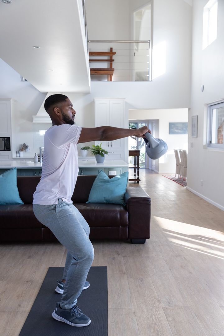 Man Performing Kettlebell Swing in Bright Living Room