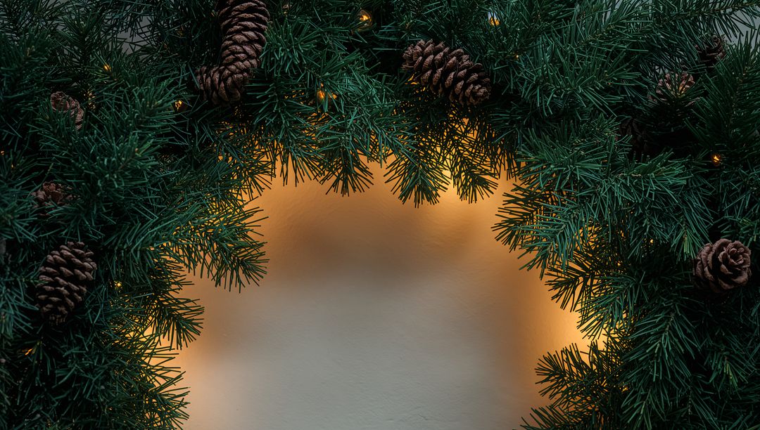 Evergreen Garland Framing Warm Amber Lights on Cream Wall with Pine Cones and Bokeh Glow