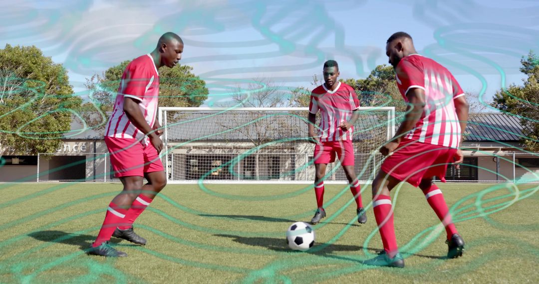 Three soccer players training on sunny grass field wearing red and white uniforms