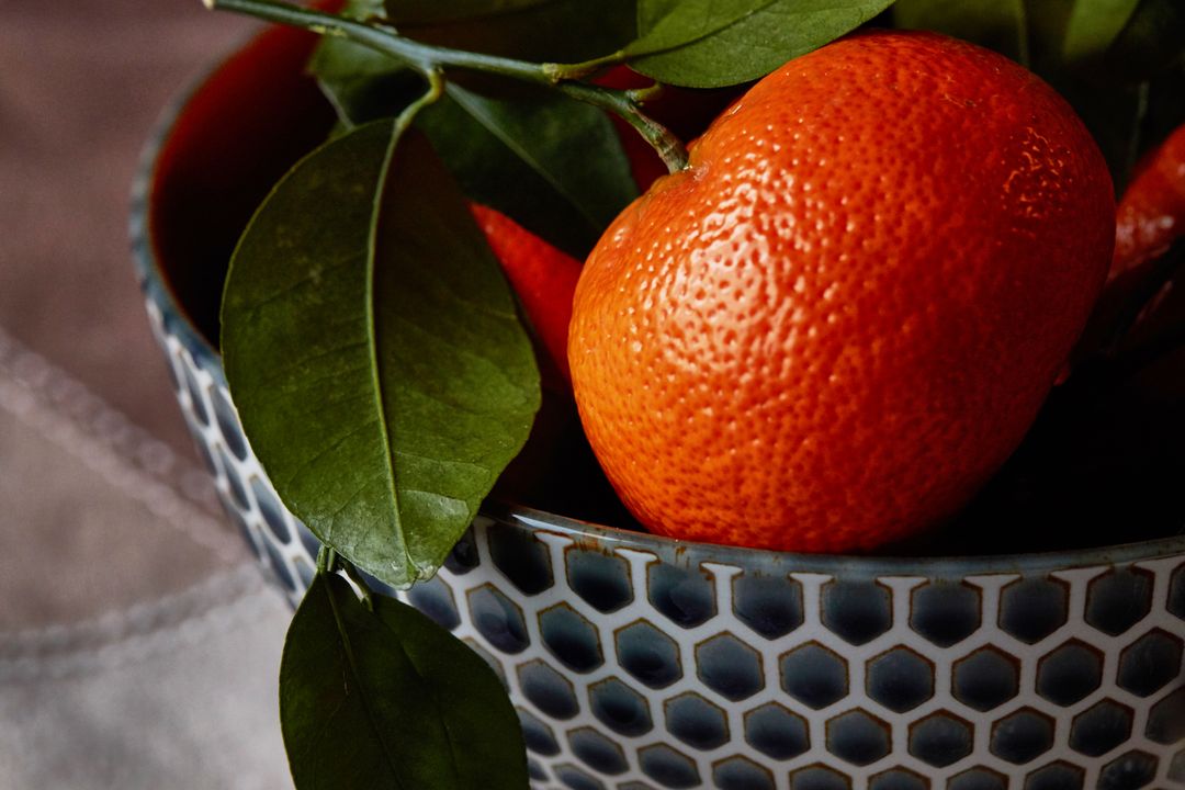 Close-up showing ripe mandarin with glossy leaves in blue honeycomb ceramic bowl