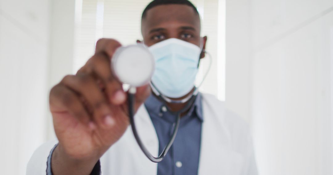 African American doctor holding stethoscope wearing mask in medical office - Free Images, Stock Photos and Pictures on Pikwizard.com