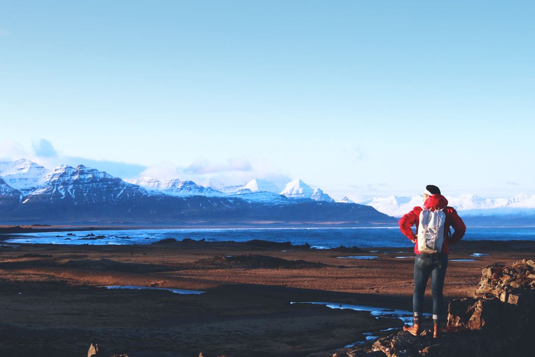Solo hiker overlooking rugged coastline and distant snow-capped mountains at golden hour