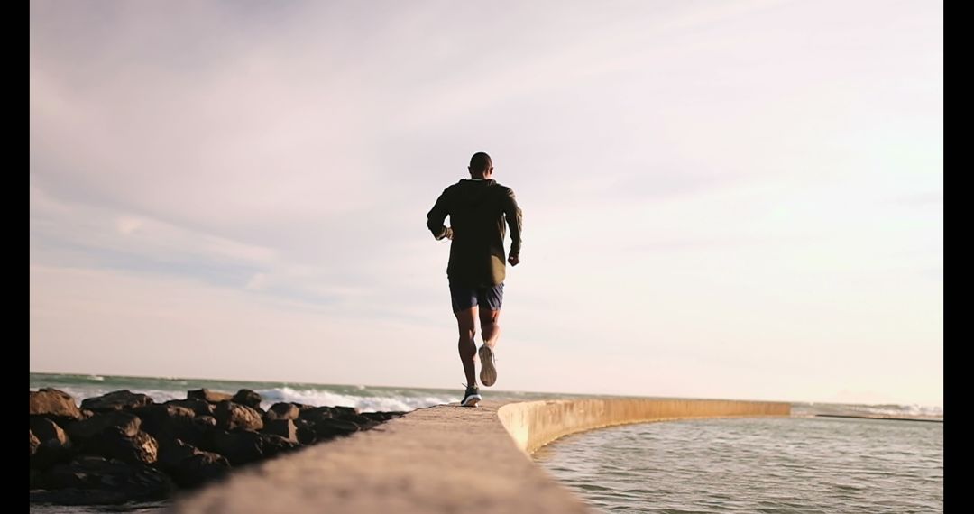Young Jogger Running on Beach Seawall by Ocean at Sunset