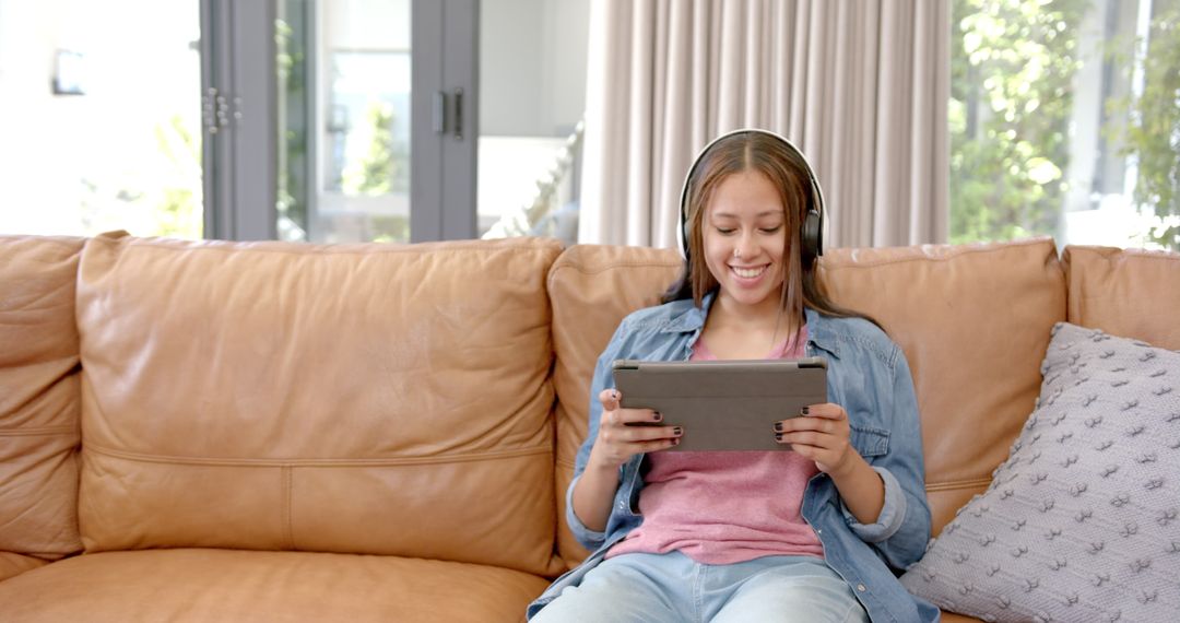 Happy Asian Woman with Headphones Using Tablet on Couch