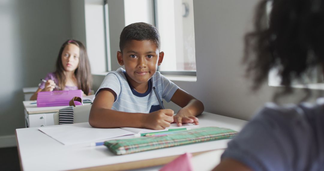 Image of happy biracial boy sitting at desk in classsroom - Free Images, Stock Photos and Pictures on Pikwizard.com
