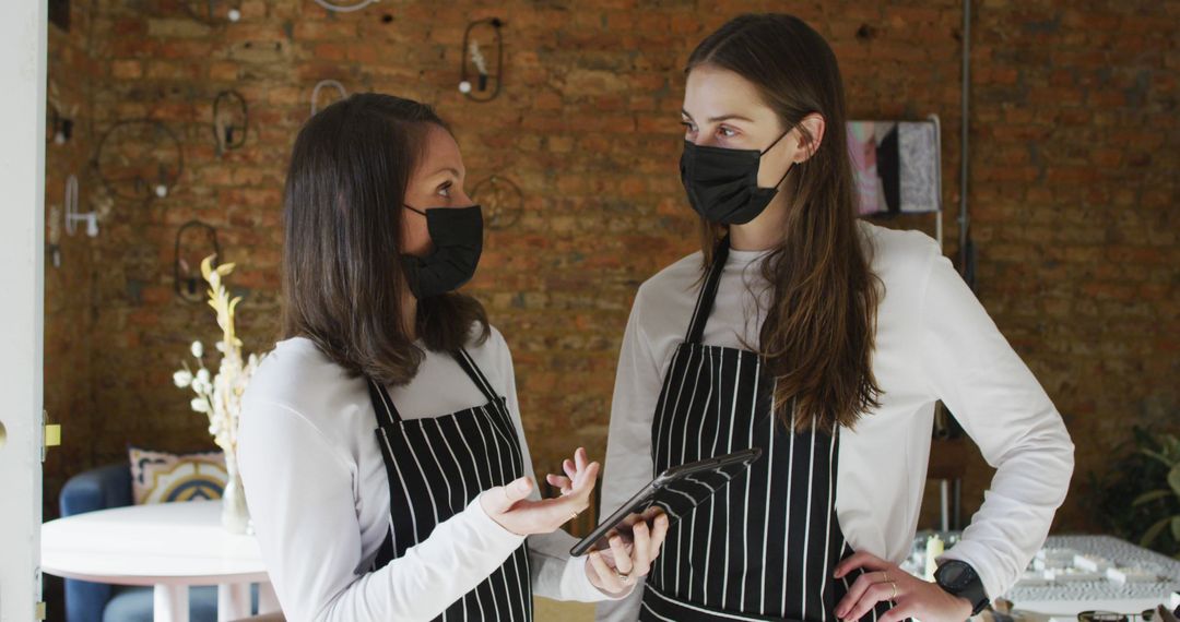 Two caucasian women wearing face masks and aprons, using tablet and talking - Free Images, Stock Photos and Pictures on Pikwizard.com