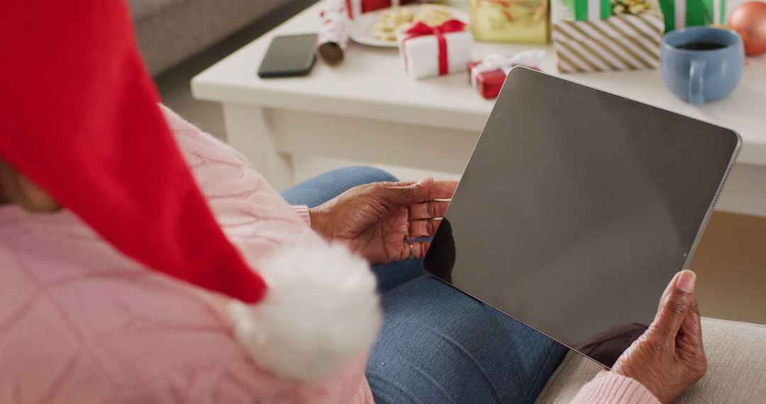 Senior Woman in Santa Hat Holding Tablet During Christmas - Free Images, Stock Photos and Pictures on Pikwizard.com