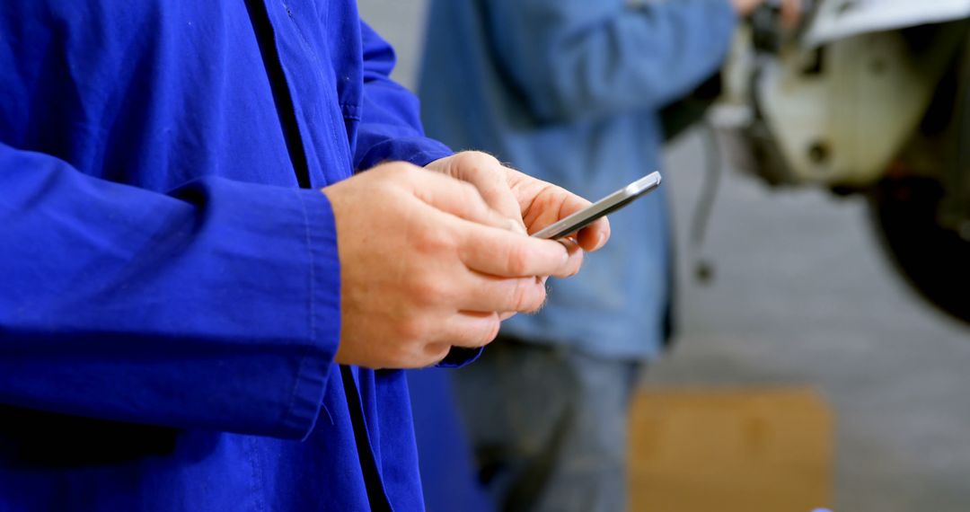 Mechanic in blue uniform using smartphone in workshop - Free Images, Stock Photos and Pictures on Pikwizard.com