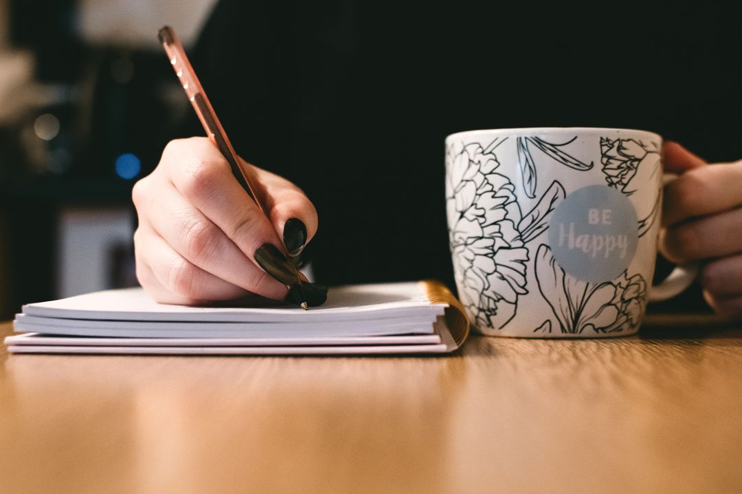 Person Writing in Journal with Coffee Mug on Table