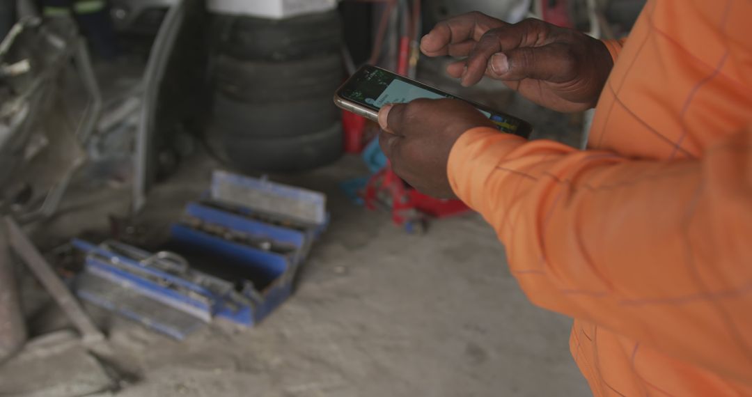 Mechanic in Orange Jacket Using Smartphone in Workshop - Free Images, Stock Photos and Pictures on Pikwizard.com