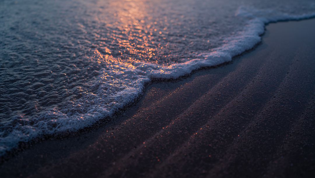 Sunset Glow Washing Over Dark Sand Shoreline with Foamy Wave and Sparkling Ripples