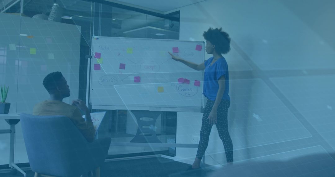 Woman presenting on whiteboard while colleague taking notes in modern office brainstorming