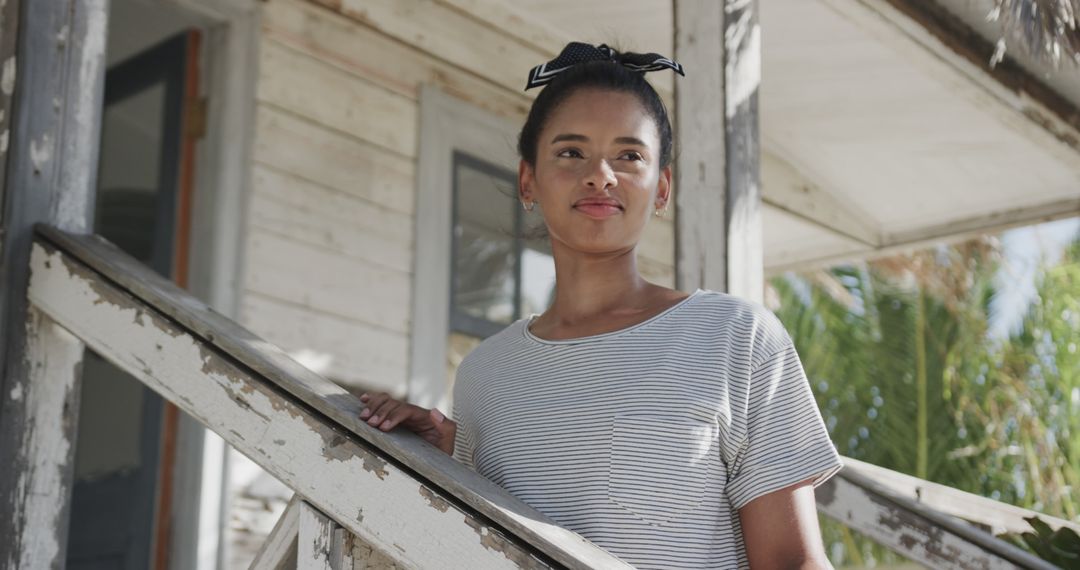 Happy biracial woman standing on stairs of house on beach - Free Images, Stock Photos and Pictures on Pikwizard.com