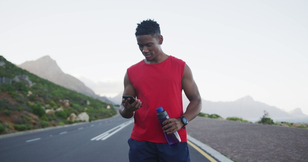 African american man holding water bottle using smartphone on the road - Free Images, Stock Photos and Pictures on Pikwizard.com