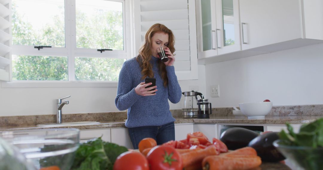 Woman Drinking Coffee while Using Smartphone in Modern Kitchen - Free Images, Stock Photos and Pictures on Pikwizard.com