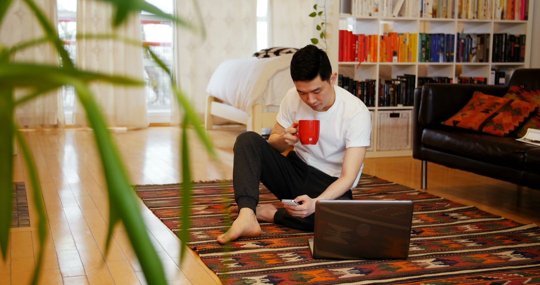 Young Man Relaxing with Coffee While Working on Laptop in Cozy Living Room - Free Images, Stock Photos and Pictures on Pikwizard.com